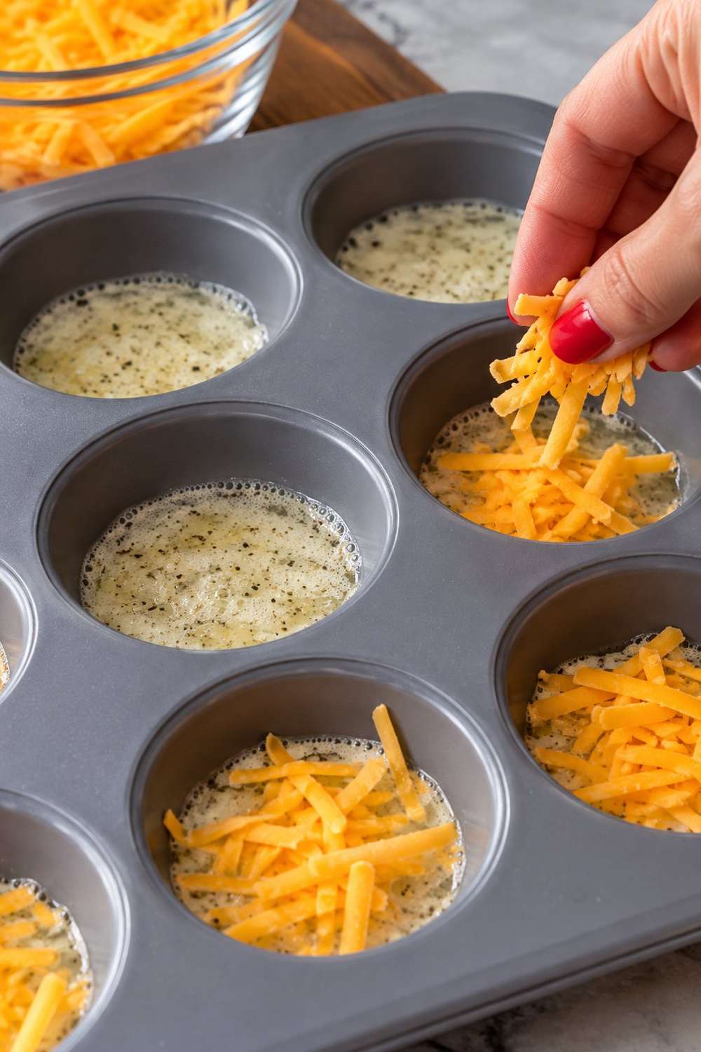 Hand sprinkling shredded cheddar over egg white mixture in muffin pan